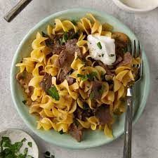 A plate of pasta with beef and sour cream on a table with a fork.