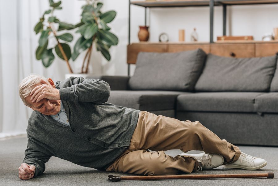 An elderly man is laying on the floor with a cane.