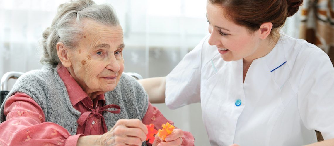 An elderly woman in a wheelchair is being helped by a nurse.