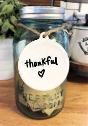 A mason jar with a thankful tag on it is sitting on a wooden table.