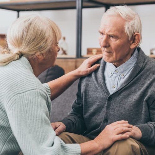 A woman is putting her hand on an older man 's shoulder.