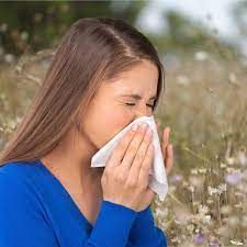 A woman is blowing her nose with a napkin in a field of flowers.