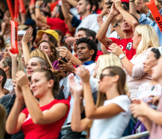 A crowd of people are sitting in a stadium with their hands in the air.