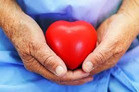 An elderly woman is holding a red heart in her hands.