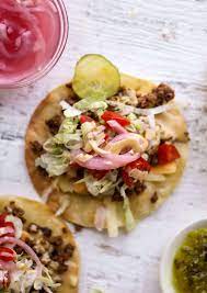 A close up of a taco with meat , lettuce , and tomatoes on a table.