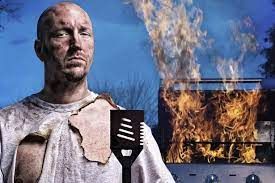 A man without a shirt is holding a spatula in front of a grill.