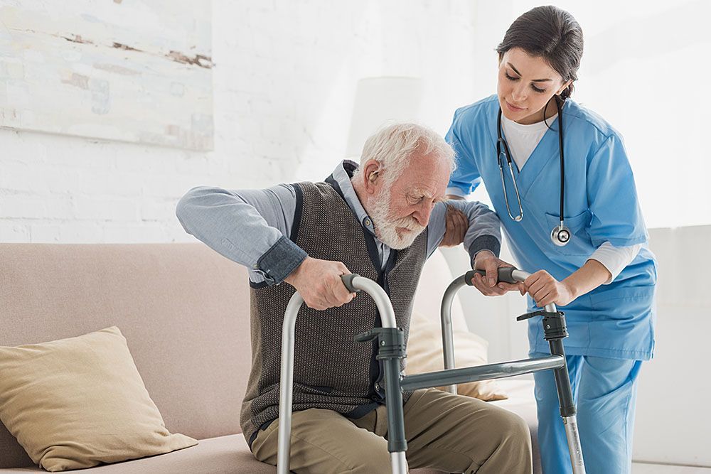 A nurse is helping an elderly man use a walker.