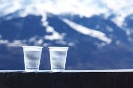 Two plastic cups are sitting on a table in front of a mountain.