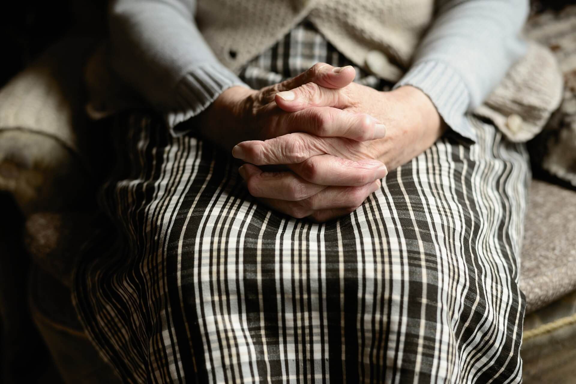 An elderly woman is sitting in a chair with her hands folded.