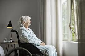 An elderly woman in a wheelchair is looking out of a window.