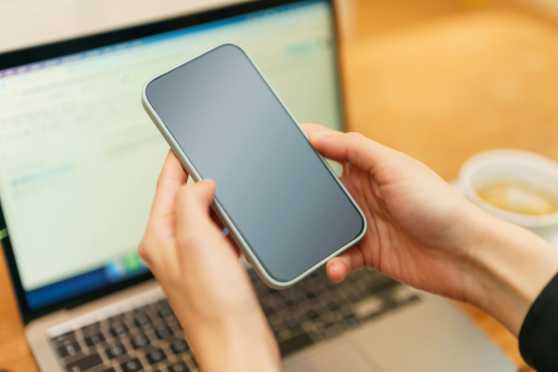 A person is holding a cell phone in front of a laptop.