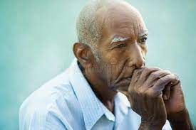 An elderly man is sitting down with his hands on his chin.