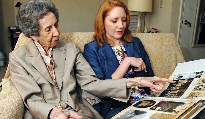 Two women are sitting on a couch looking at a photo album.