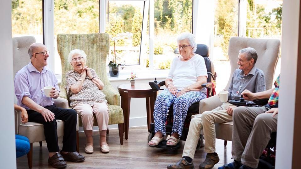 A group of elderly people are sitting in chairs in an elderly care home.