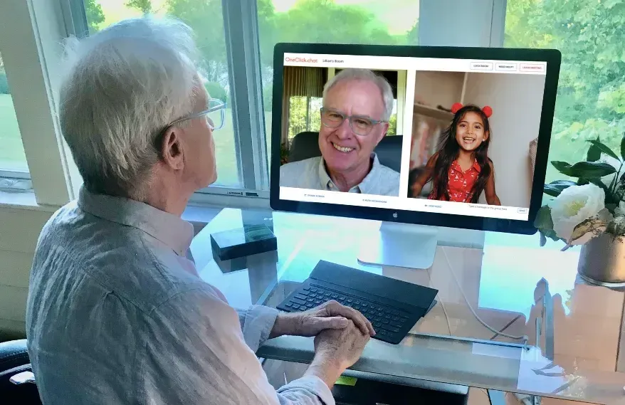 An elderly man is sitting at a desk using a computer.