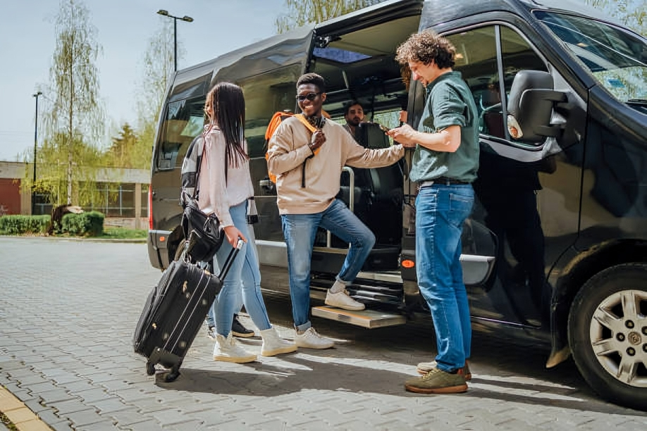 People boarding a black van. One holds a phone; others carry bags, wearing casual clothing outdoors.