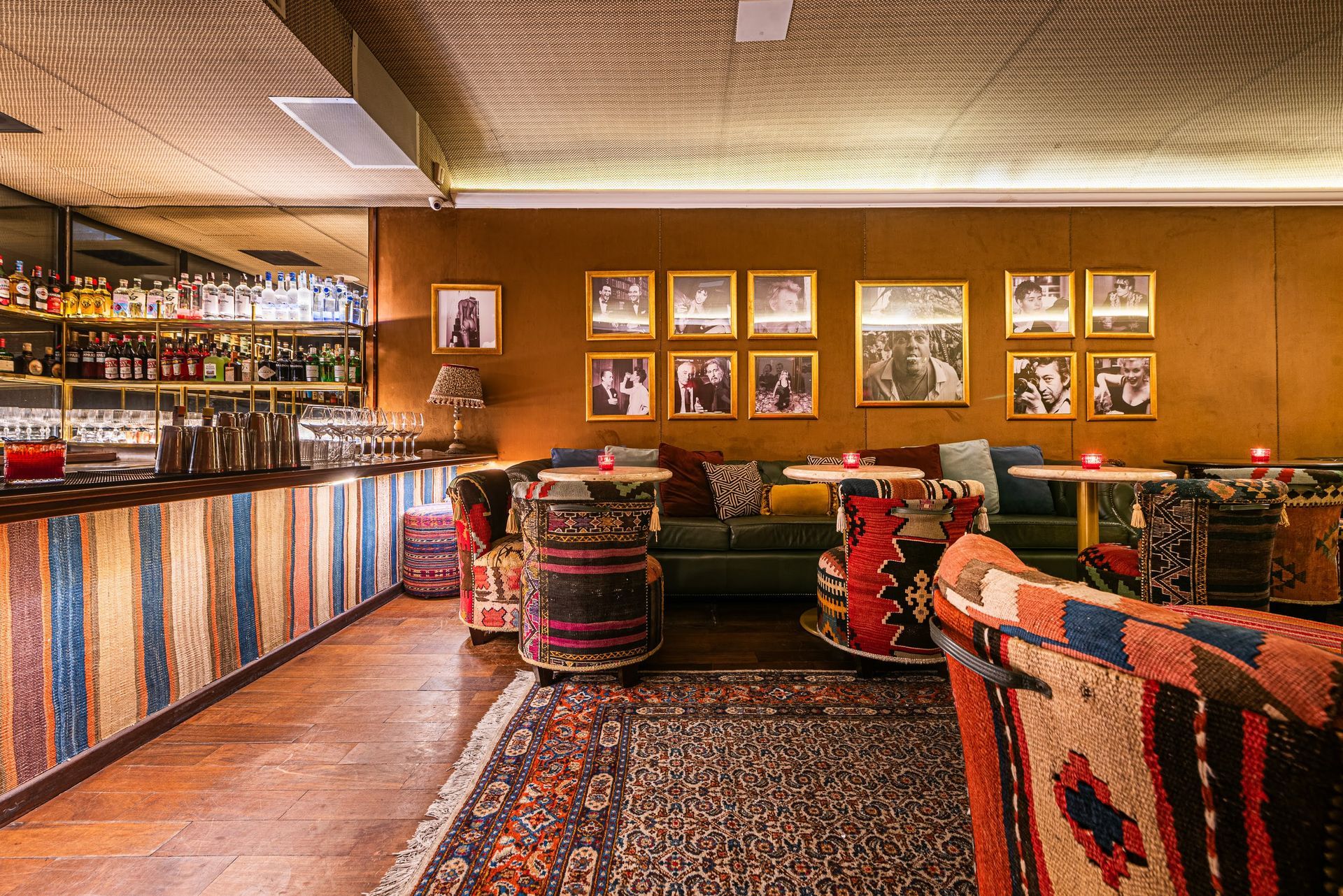 Bar aconchegante com cadeiras estampadas, balcão de madeira e obras de arte emolduradas na parede, sob iluminação quente.