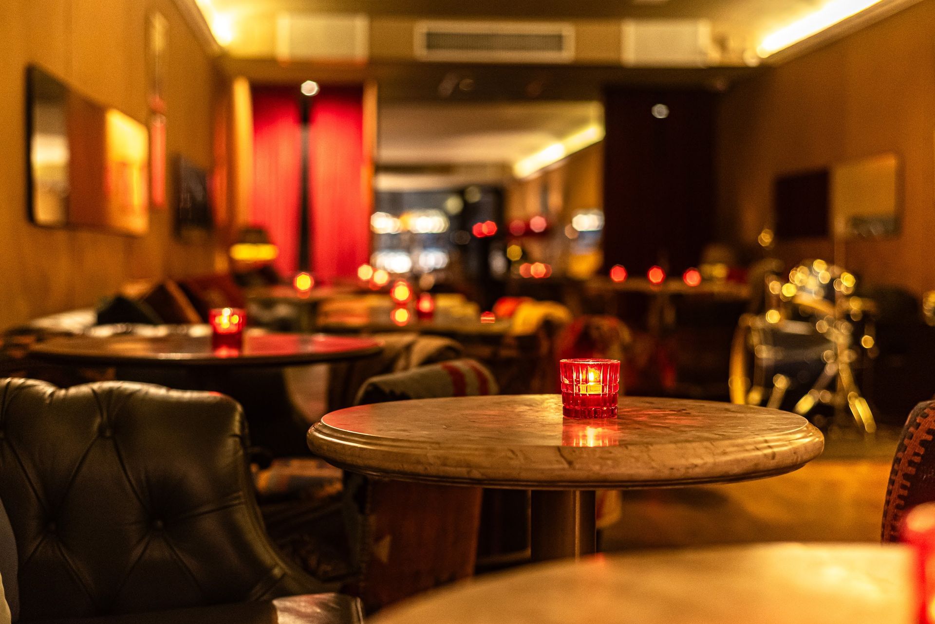 Sala de estar com iluminação suave, poltronas de couro, mesinhas e luz quente de velas vermelhas.