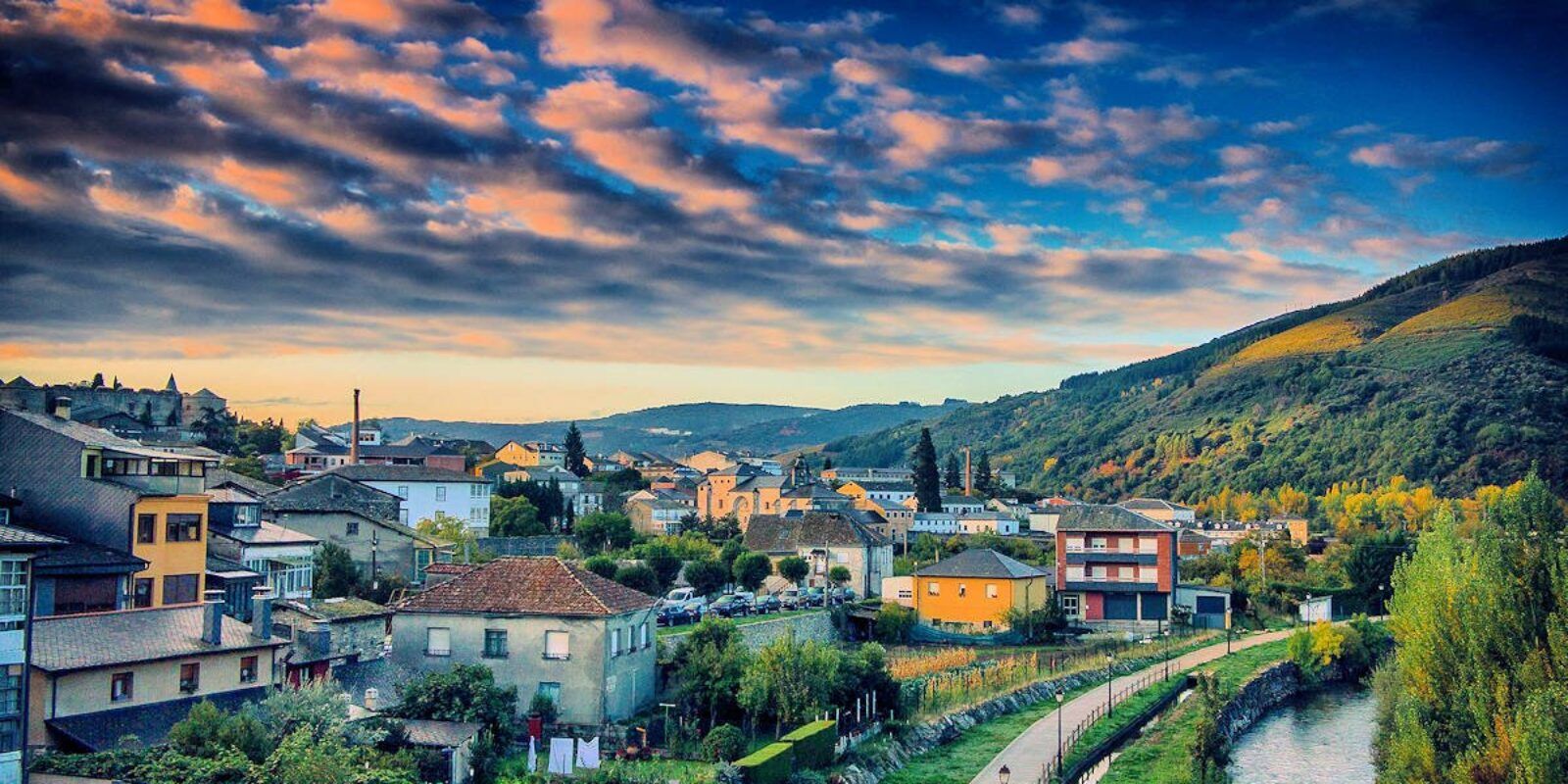 Town nestled in valley with green hills, blue sky, and colorful sunset.
