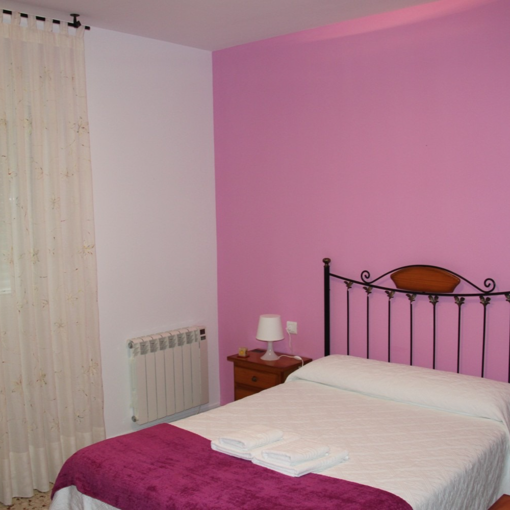 Bedroom with white bed, purple blanket, pink wall, small nightstand, and radiator.