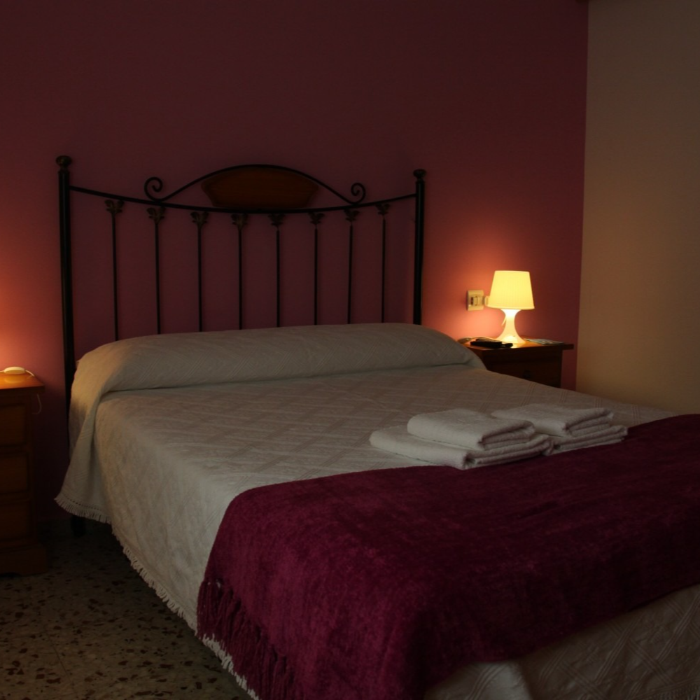 Bedroom with a made bed, nightstands, lamps, and a dark pink wall.