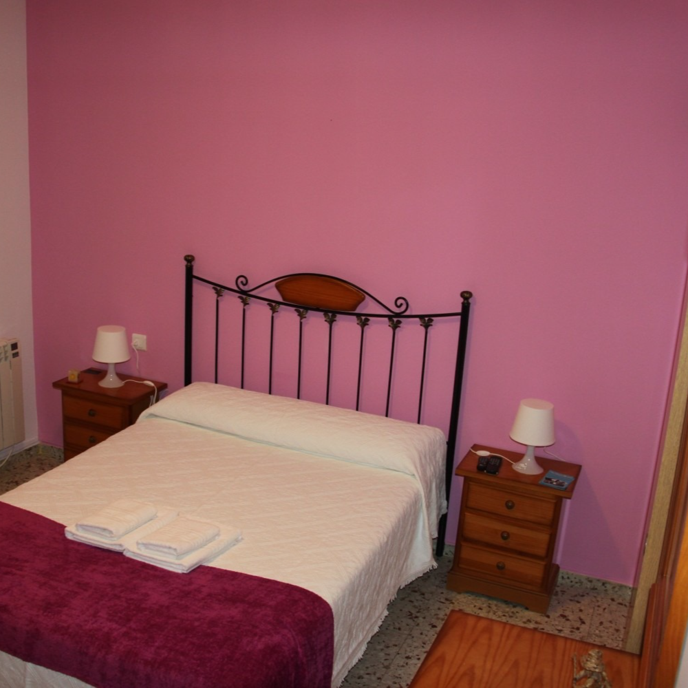 Bedroom with a double bed, dark metal headboard, pink walls, and two wooden nightstands.
