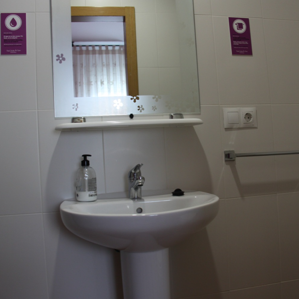 Bathroom with white pedestal sink, mirror, soap dispenser, and towel rack on a tiled wall.