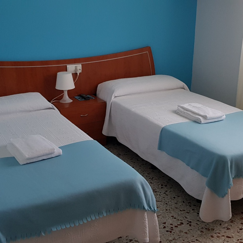 Two twin beds with blue blankets, white sheets, and towels in a hotel room with blue walls.