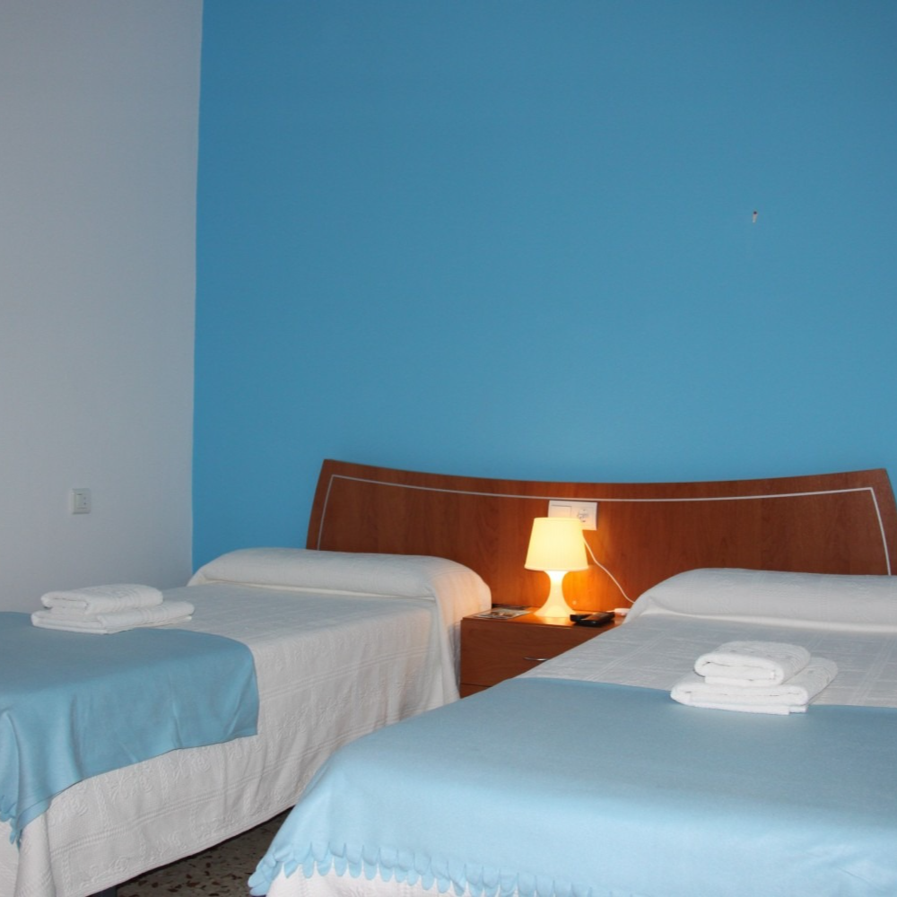 A hotel room with three beds, a nightstand, and a blue accent wall.