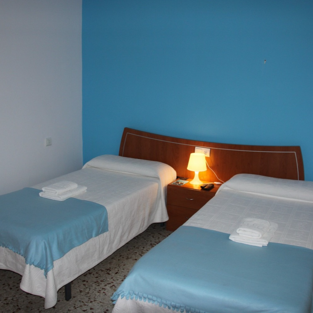 Two twin beds in a room with blue and white walls and a bedside lamp.