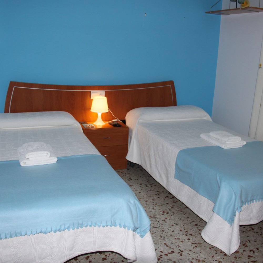 Two beds in a room, blue walls, a lamp on a nightstand, and white towels.