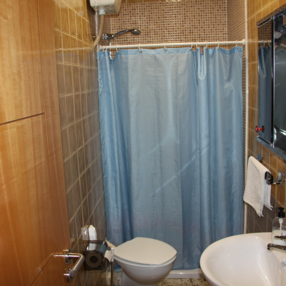 Small bathroom with brown tile walls, toilet, sink, blue shower curtain, and a wall cabinet.