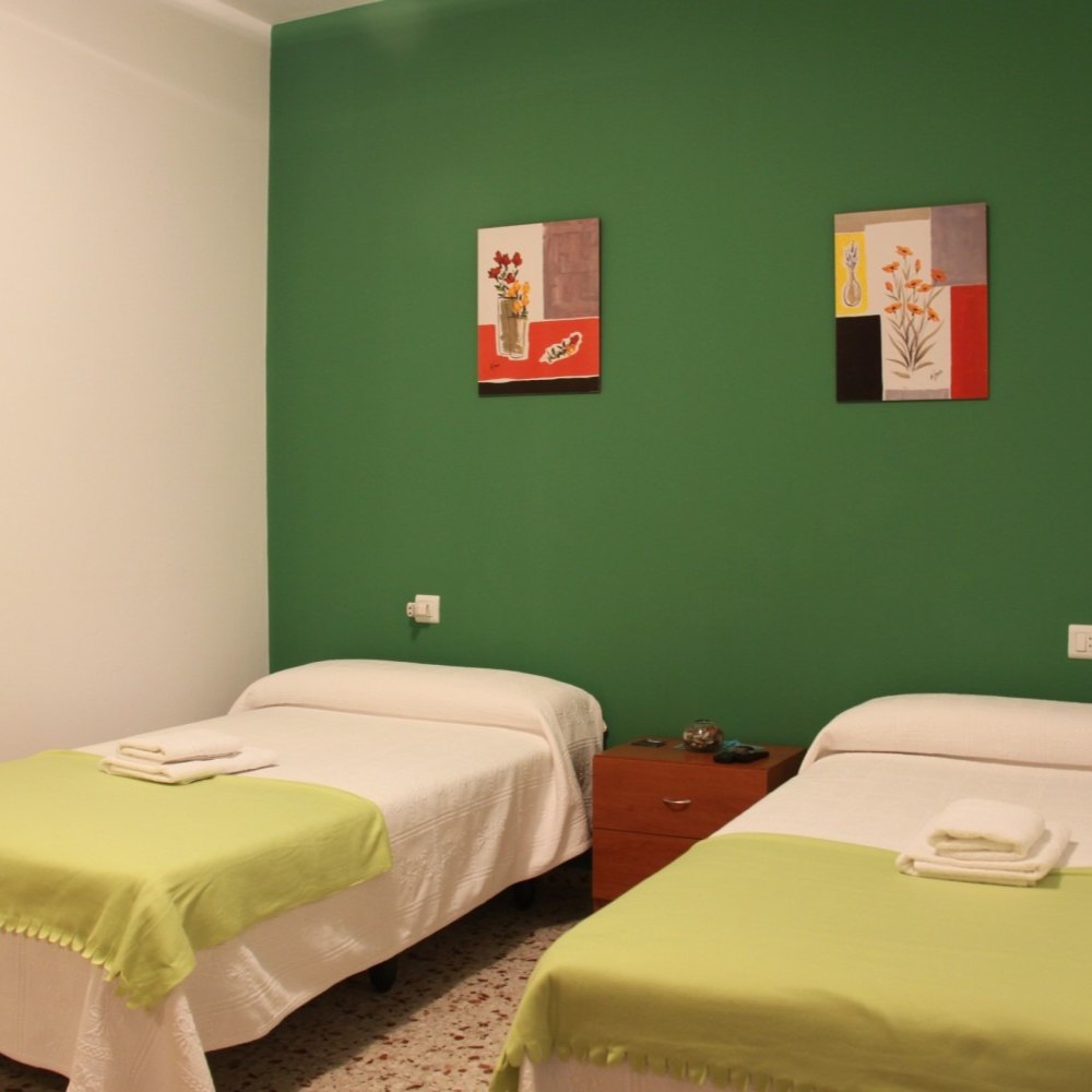 Two twin beds with green blankets and art on a green wall.