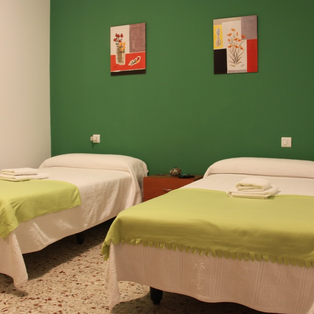 Two twin beds in a room with green and white walls, artwork and a red nightstand.