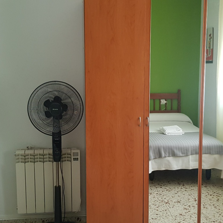 Tall orange closet with a mirror reflects a bed, green wall, and fan.