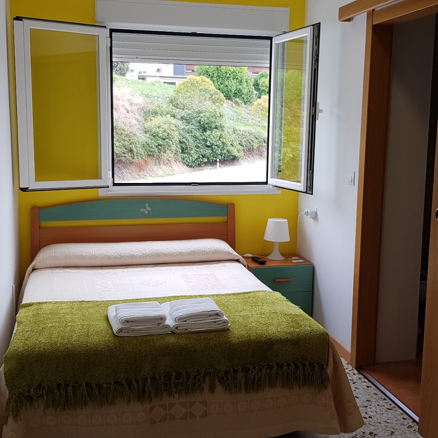 Bedroom with a bed, nightstand, and window overlooking greenery; yellow walls, white trim.