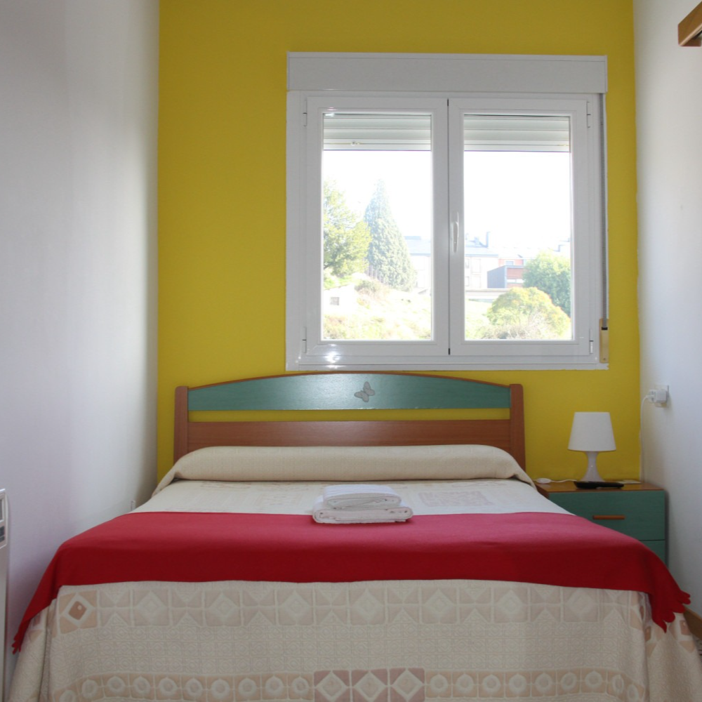 Bedroom with yellow walls, bed with red cover, window, and small nightstand.
