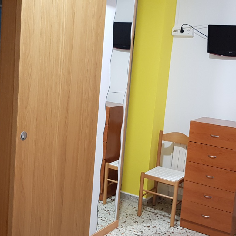 Wooden wardrobe with mirror, chest of drawers, chair, and two TVs in a room with yellow and white walls.
