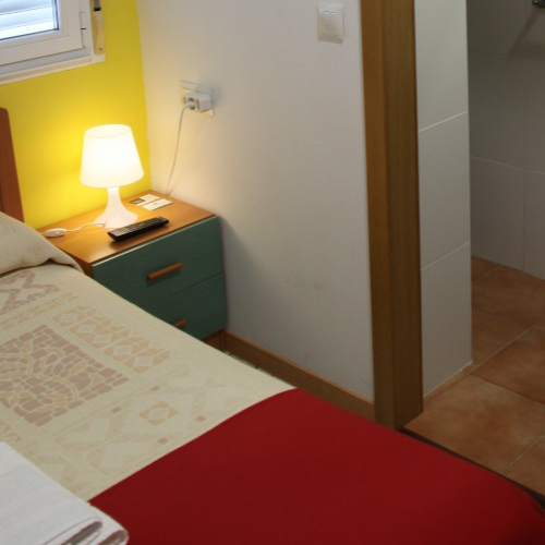 Bedroom with a red bedspread, nightstand, lamp, and open door to bathroom.