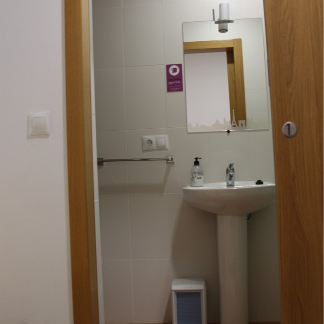 Bathroom with a pedestal sink, mirror, towel bar, and trash can. The door frame is visible.