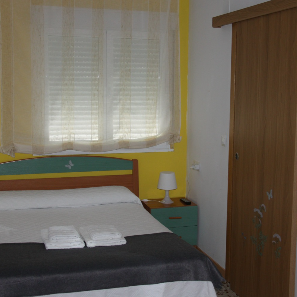 Bedroom with a bed, bedside table, window with blinds, and wooden wardrobe.