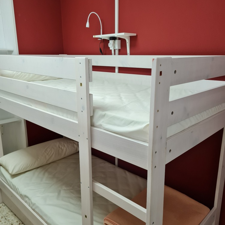 White bunk beds against a red wall with a reading light and blanket.