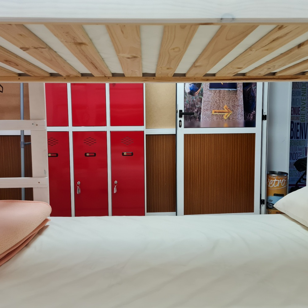 View from a lower bunk bed of red lockers, a door with a sign, and the bed above.