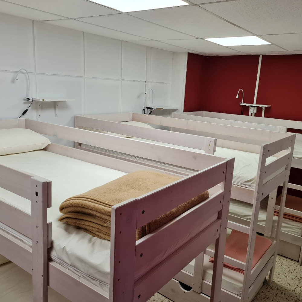 Bunk beds in a room with white walls and a red accent wall; a blanket rests on a bed.