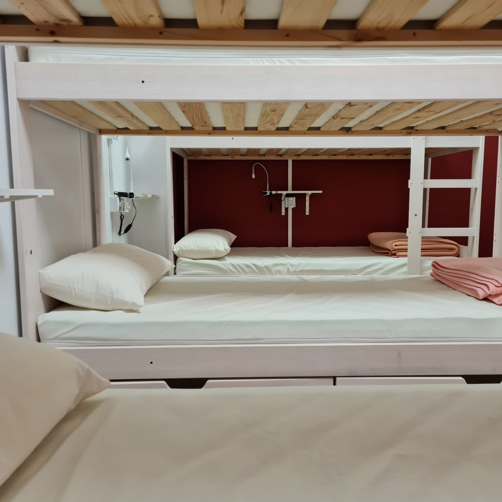 Bunk beds in a room. White beds and frame with red back wall. Includes pillows, blankets and a light.