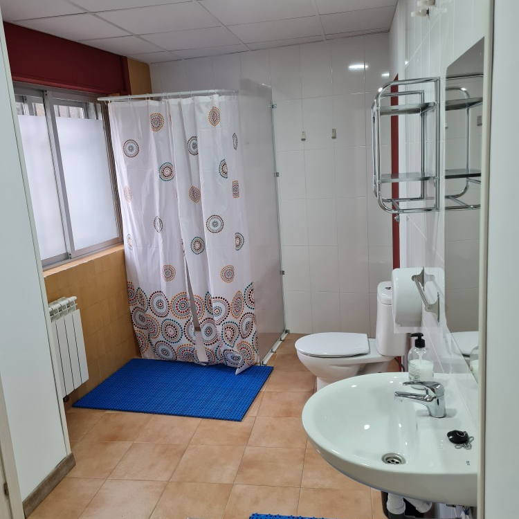 Bathroom with a shower curtain, toilet, sink, and window. Blue mat on floor.