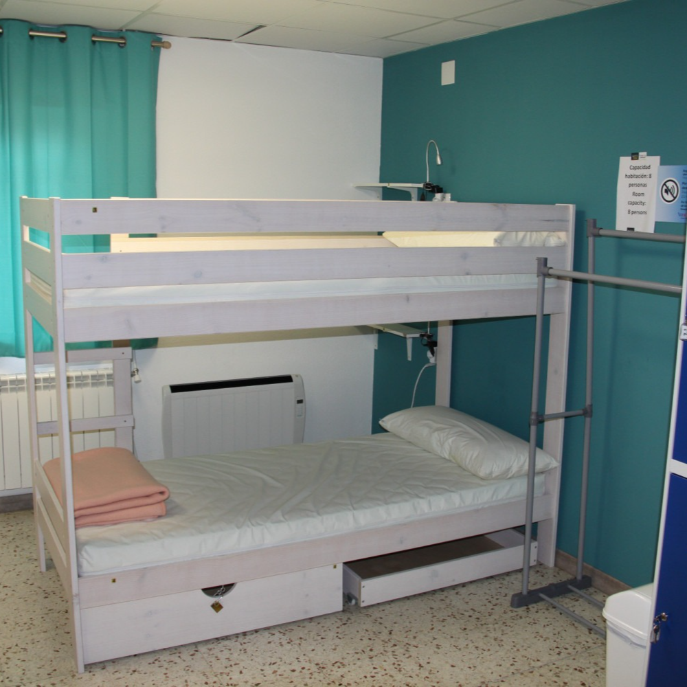 Bunk bed in a room with teal walls. Bottom bed made, top bed unmade. Pink blanket on lower bed.