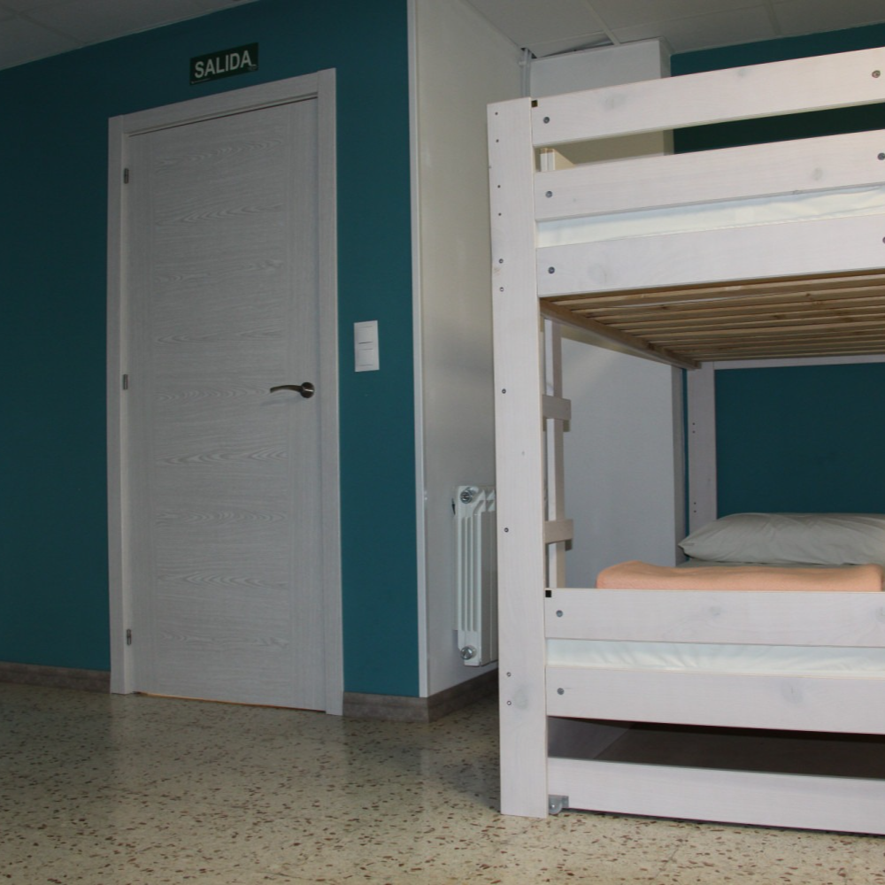 Bunk beds in a room with blue wall, white door, and exit sign. Light brown tiled floor.