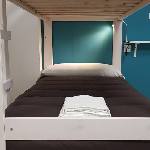 Bunk bed with brown mattress, white towel, teal wall, and wooden frame.