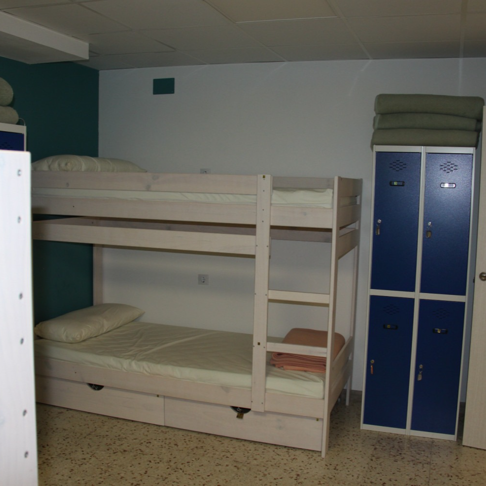 Bunk beds and lockers in a hostel dorm room; white, blue, and green colors.